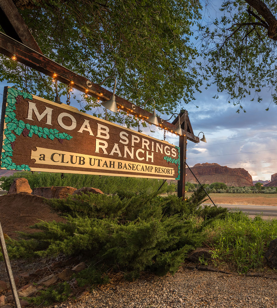 The Moab Springs Ranch corporate logo is a large wooden rectangular sign placed by the roadside illuminated by sign lamps for arriving guests.