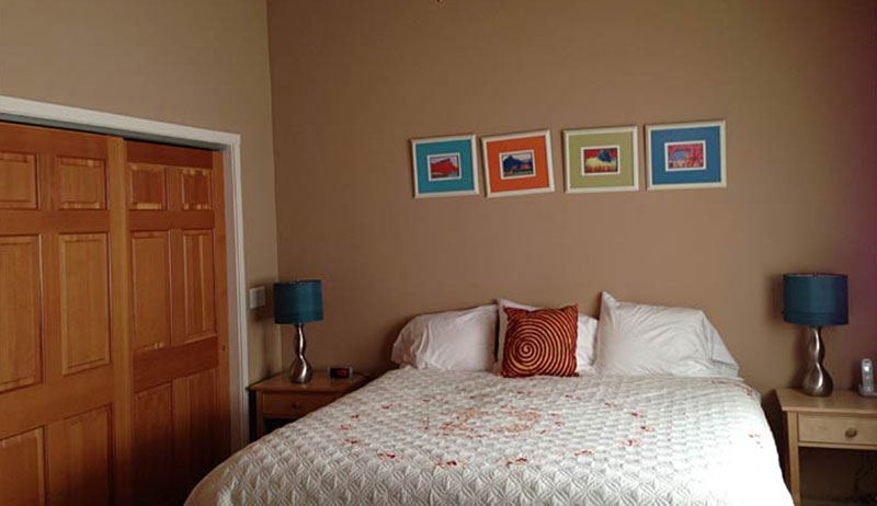 Four small multi colored framed pictures hang over a bed dressed in a quilted white cover with two bedside tables at a townhouse suite at Moab Springs.