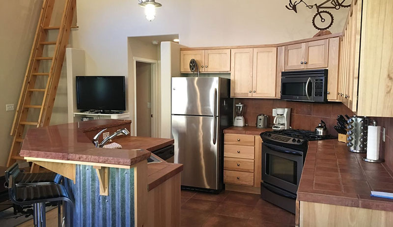 The kitchen of Unit #21 at Moab Springs Ranch is fully equipped with a wrap around island serving as a breakfast bar, full sized stainless steel refrigerator, gas stove and flat screen TV.