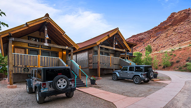 A bungalow unit made entirely of brown wood slats features large woodframed windows, a spacious porch and a sturdy staircase at Moab Springs Ranch.