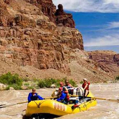 A small photograph of adventurers on a yellow inflatable raft, riding the rapids of the Colorado River with towering rusty brown sandcliffs in the background.