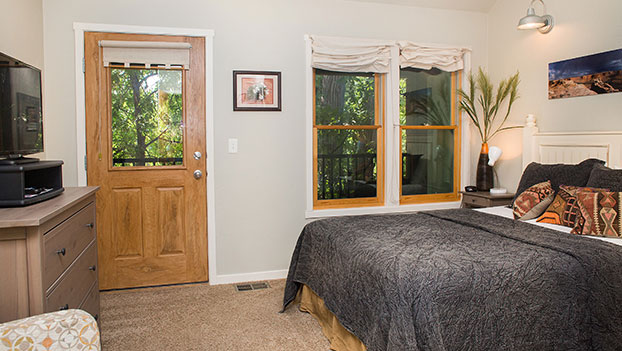 A townhouse bedroom suite at Moab Springs Ranch features a king sized bed with a multi-colored circular pattern covering and two white bedside tables with lamps.