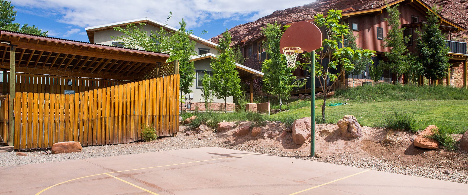 The recreation area of Moab Springs Ranch features a basketball court with in-ground pole and hoop and the whirlpool area enclosed by wood slat fences and covered by a slanted wood roof.