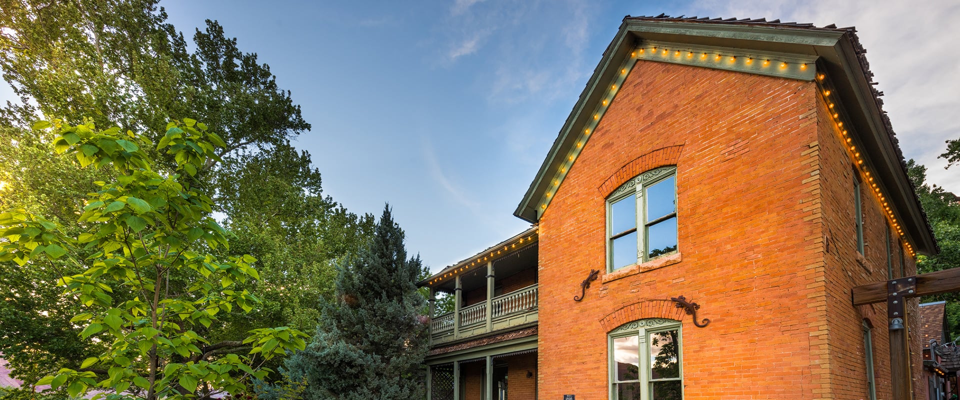 Upward view of the red-orange brick National Historic Register Ranch House at Moab Springs Ranch and the surrounding green foliage and towering cottonwood trees.