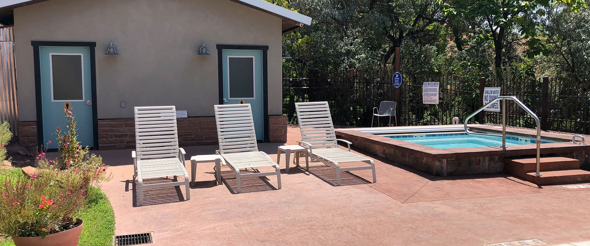 Four sets of black wrought iron tables and chairs are placed over red and white stone pavement at an outdoor seating area for guests of Moab Springs Ranch.