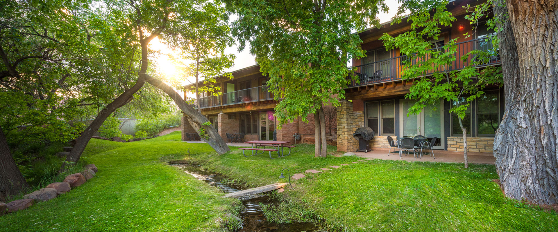 A man-made stream runs by lounge chairs, picnic tables, hammocks and tall cottonwood trees in the green parkspace at Moab Springs Ranch in Utah.