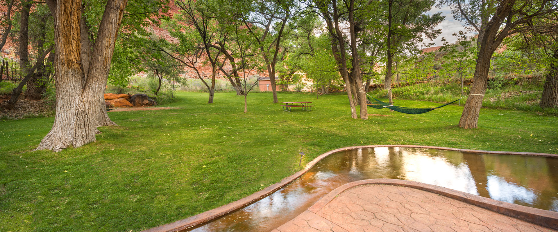 A white loveseat swing set, made of wood slats is set against the background of a ranch style fence and the looming sandstone mountain cliffs of Moab, Utah.