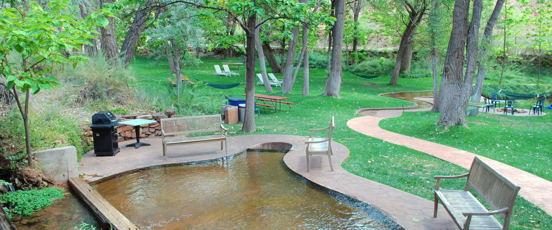 Clusters of purple wisteria hang over a steel rod fence enclosing a lounge area with a chaise lounge, patio seats, and filigree ironwork tables at Moab Springs Ranch.