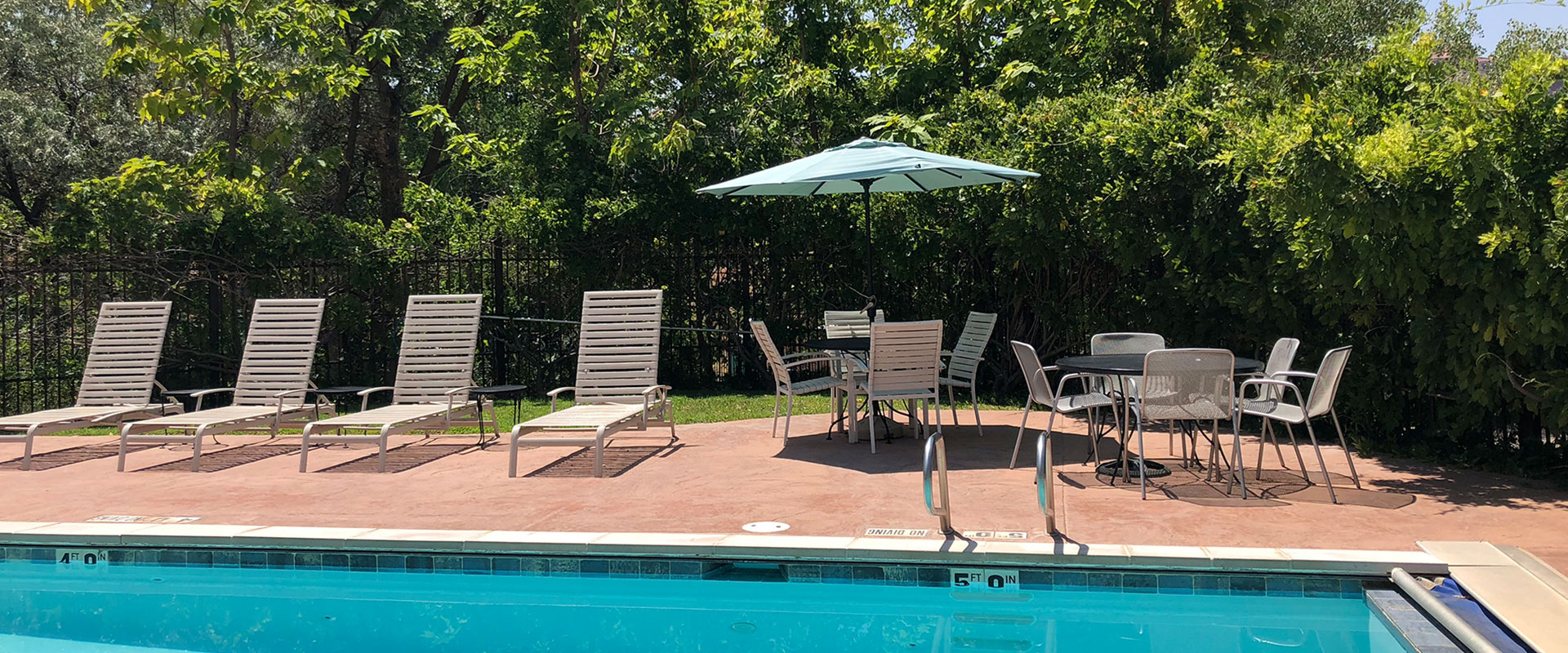 The swimming pool area at Moab Springs Ranch is surrounded by black steel rod fencing with multitudes of purple wisteria flowers lazily dangling over.