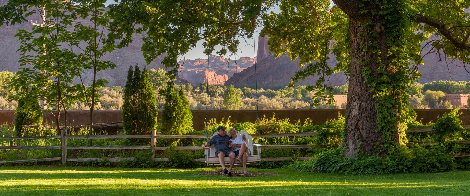 Tree branches full of lush green leaves hover over a pond and are reflected in the shallow water at Moab Springs Ranch in Utah.