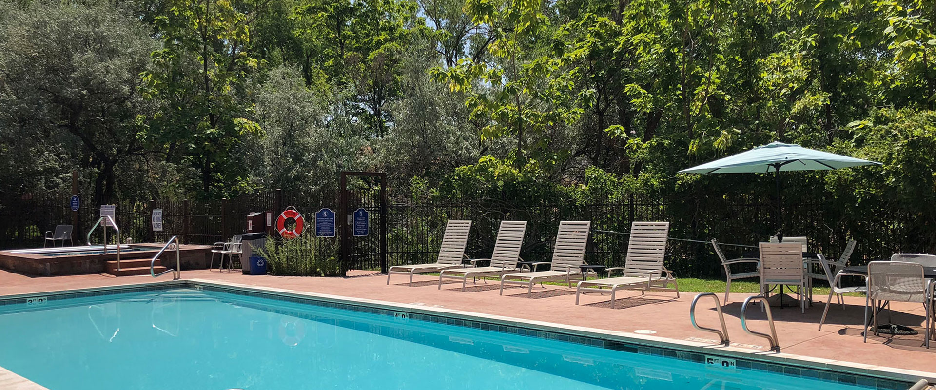 A blonde female child in a bathing suit twirling a hula hoop, plays in the man-made stream against the natural backdrop of green grass and trees at Moab Springs Ranch.