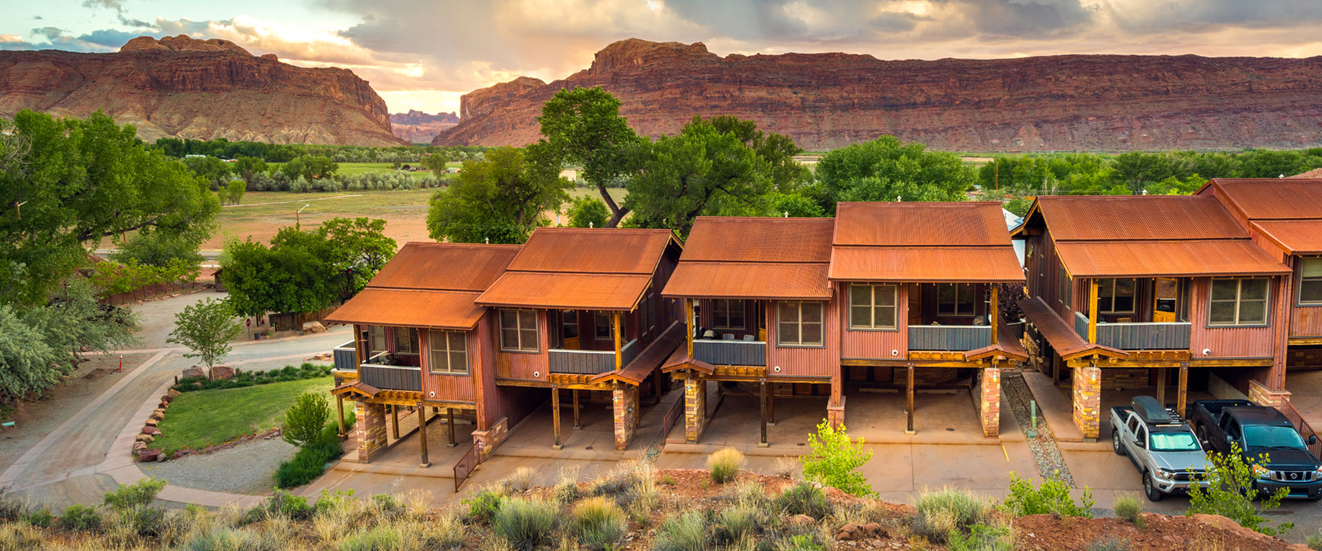 The Moab Springs Ranch sign faces oppposite an empty road, a view of the vast grasslands and towering sandstone mountain cliffs of Moab, Utah.