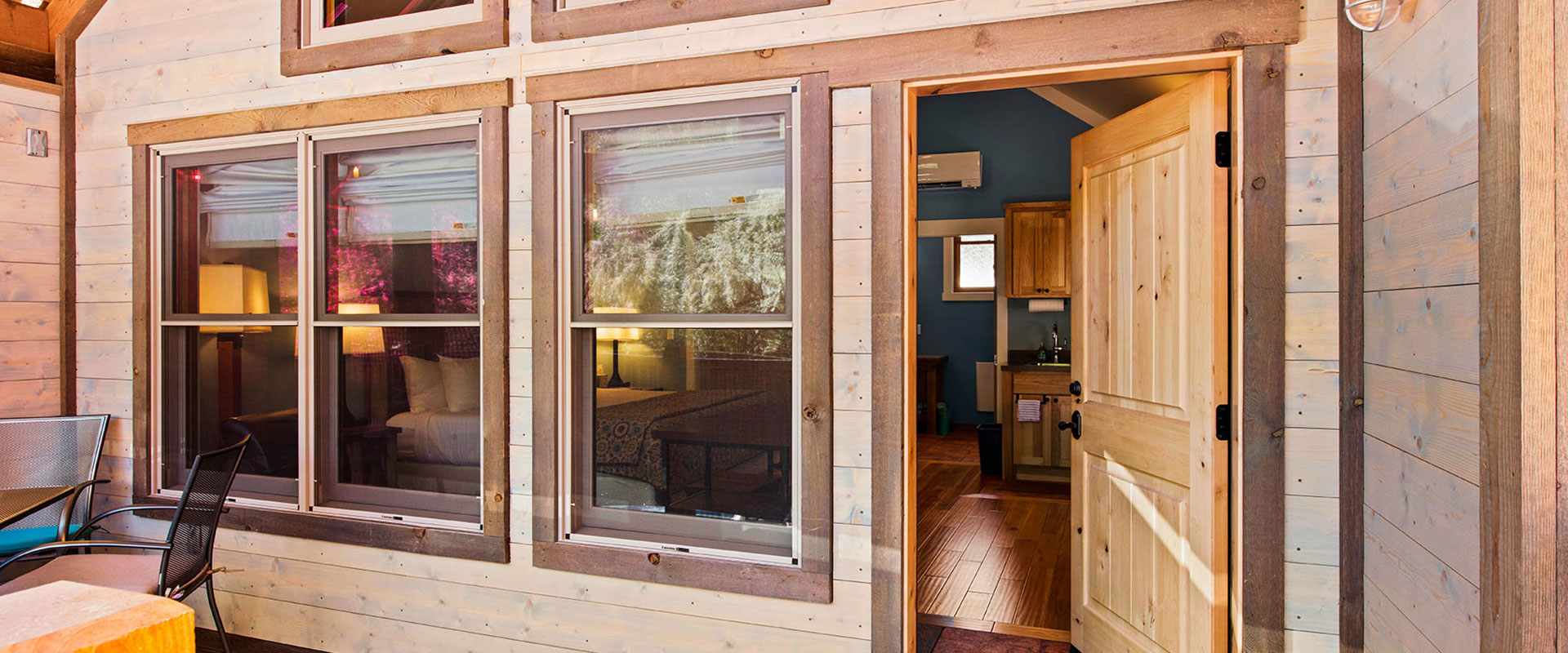 Balcony view from a unit at Moab Springs Ranch overlooking green and plum colored trees, the corrugated roofs of neighboring units and towering sandcliffs in the background.