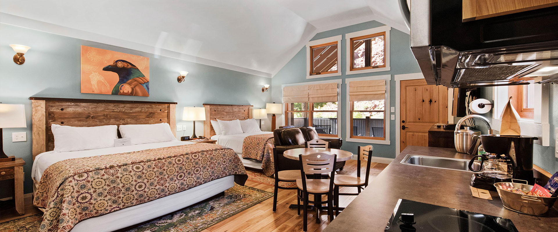 The bedroom of Unit #19 at Moab Springs Ranch is furnished with a king sized bed with a circular geometric print cover, a solid brown wood headboard and white bedside tables.