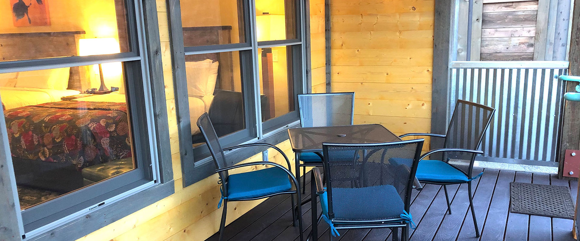 The outdoor space of a housing unit on Moab Springs Ranch has sturdy metal chairs and table, a black woodburning fireplace, barbecue and corrugated metal enclosure.