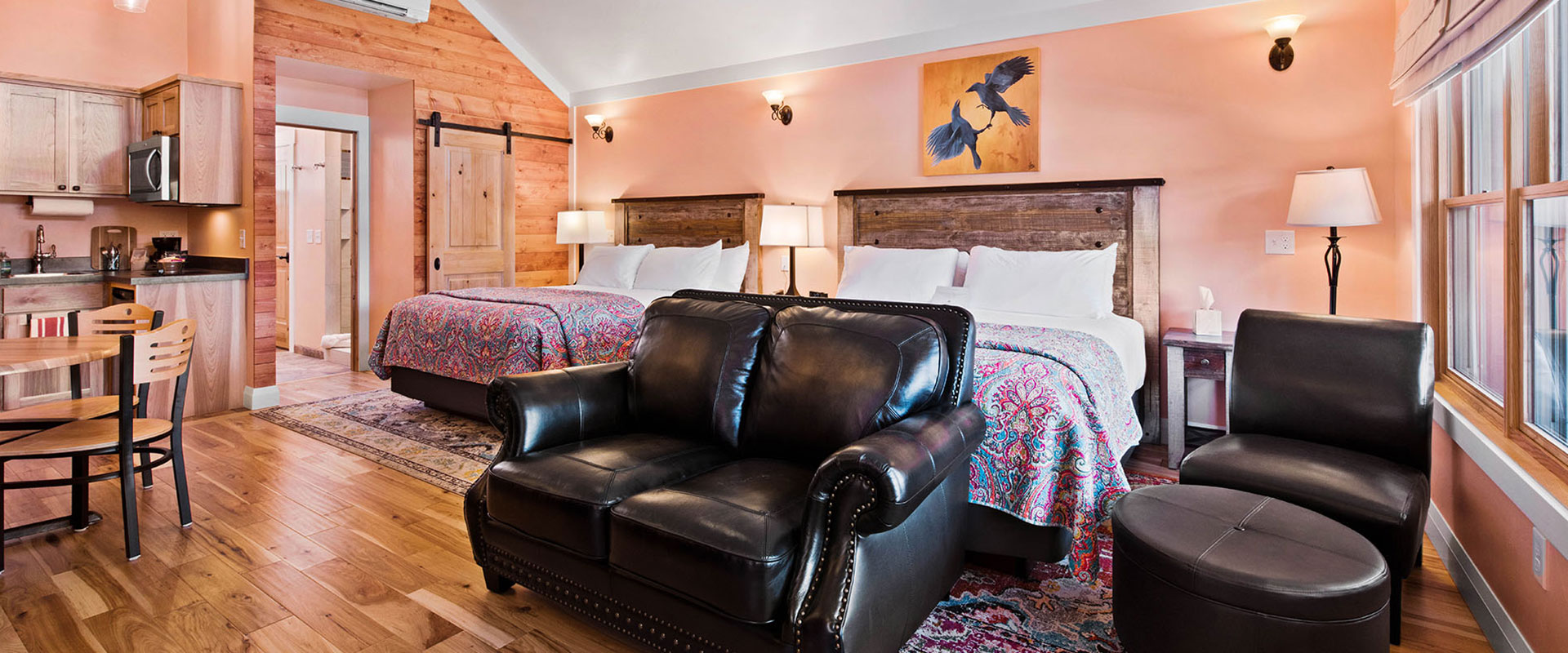 A large bed dressed in green, blue and white print linen is placed beside a large woodframed window with views of tall cottonwood trees at the Moab Springs Ranch property.