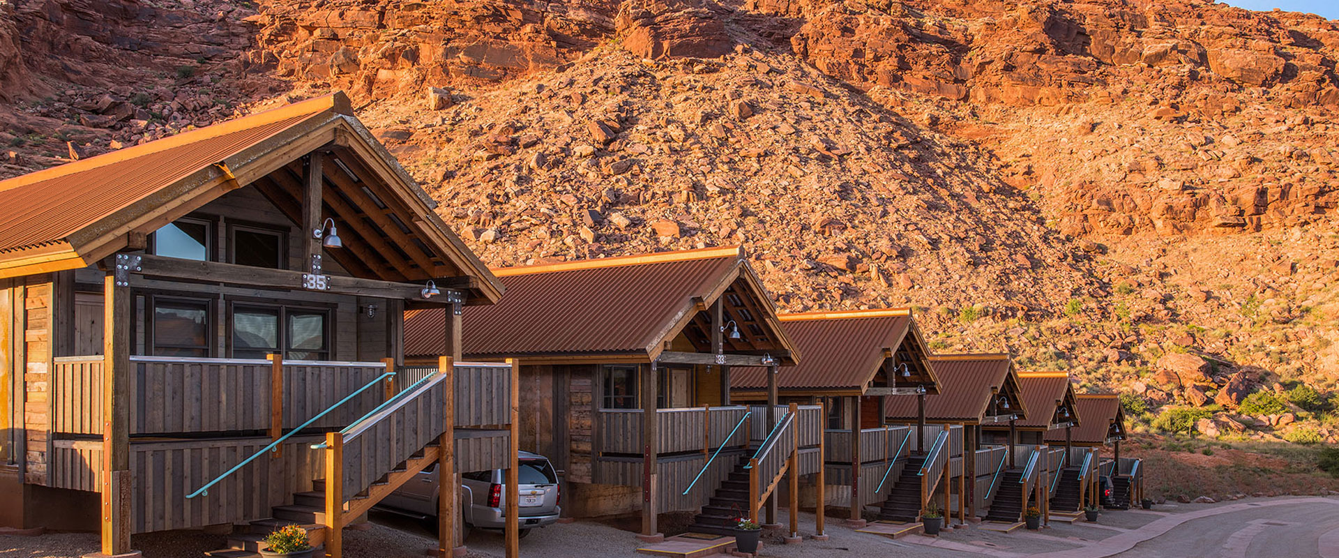 Rows of triangular rooftops of townhouses at Moab Springs Ranch are set against the background of sandcliffs, pale green grasslands and tall lush cottonwood trees.