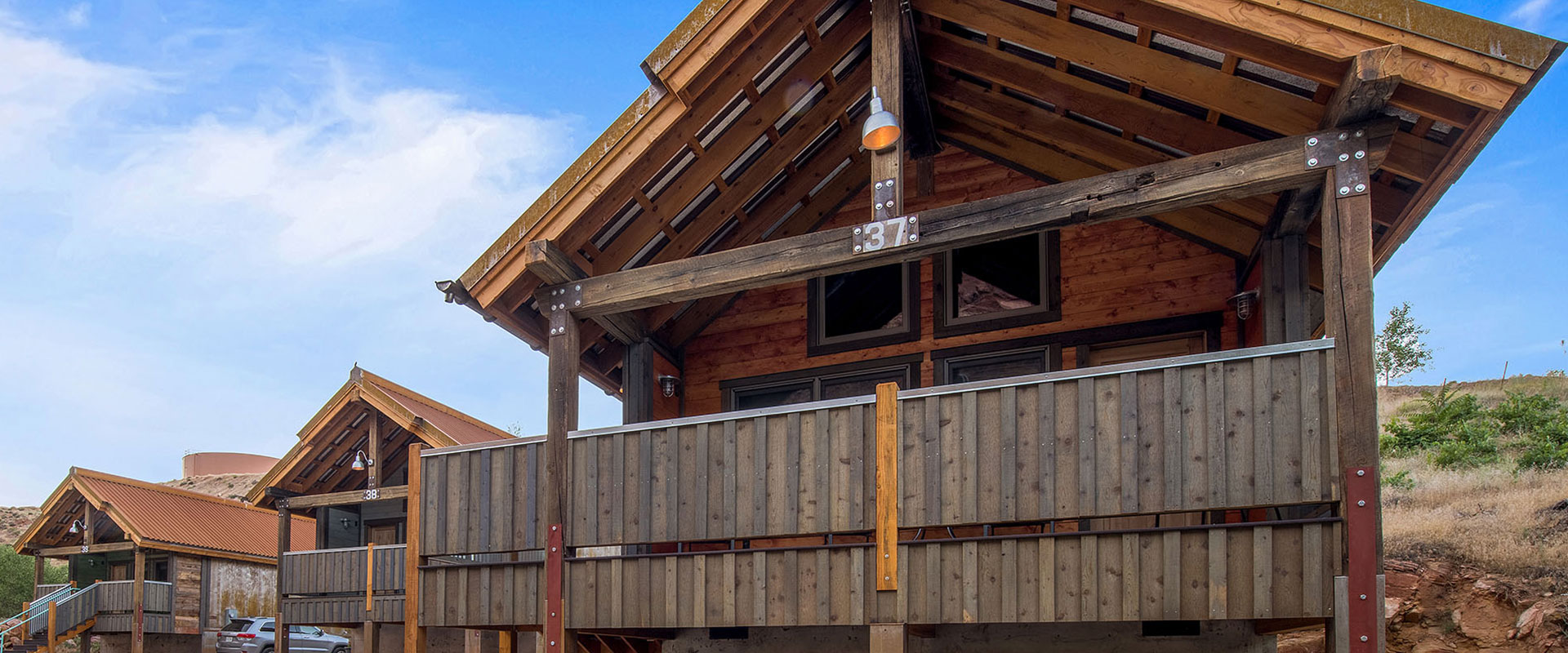The outdoor lounging area of townhomes at Moab Springs Ranch faces a shallow stream, vibrant green grassland and towering cottonwood trees.