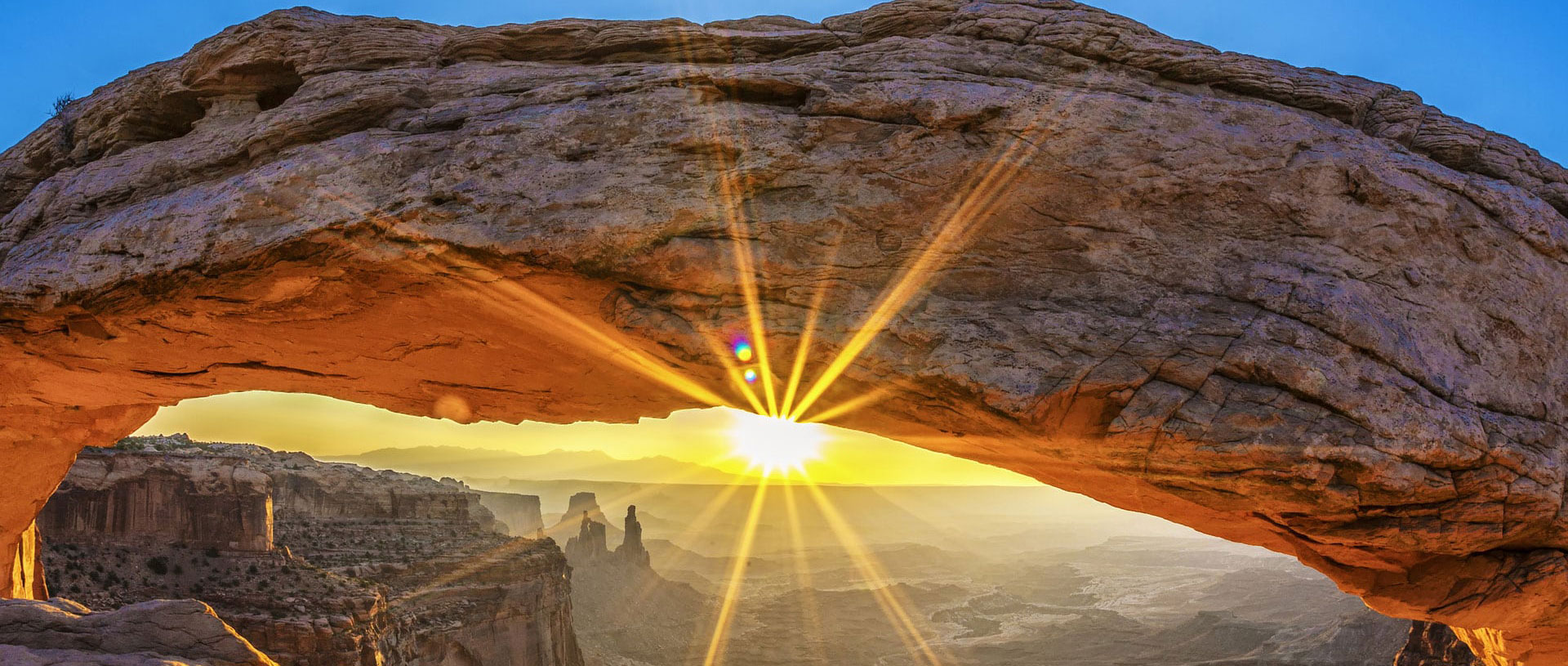 The underside of a naturally formed sandstone arch framing the view of sandstone cliffs, valleys and brilliant sunset at Arches National Park in Moab, Utah.