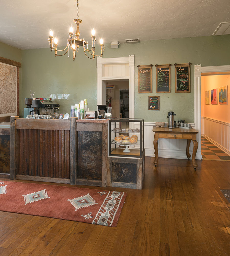 The Main House at Moab Springs Ranch is a two story brown brick structure that sits amongst lush tall trees with multi-colored vegetation at its' doorstep.