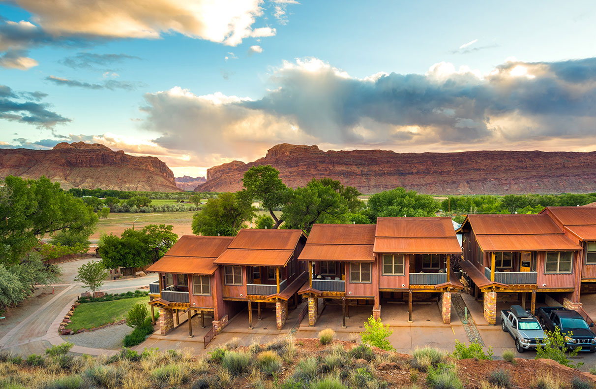 A man-made stream runs across the parkspace of Moab Springs Ranch with towering green trees, a hammock and a picnic table in the background.