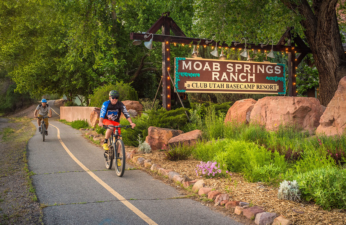 The private park space at Moab Springs Ranch features a stream, a man-made pond, a paved coral brick path and a network of tree foliage providing shade.