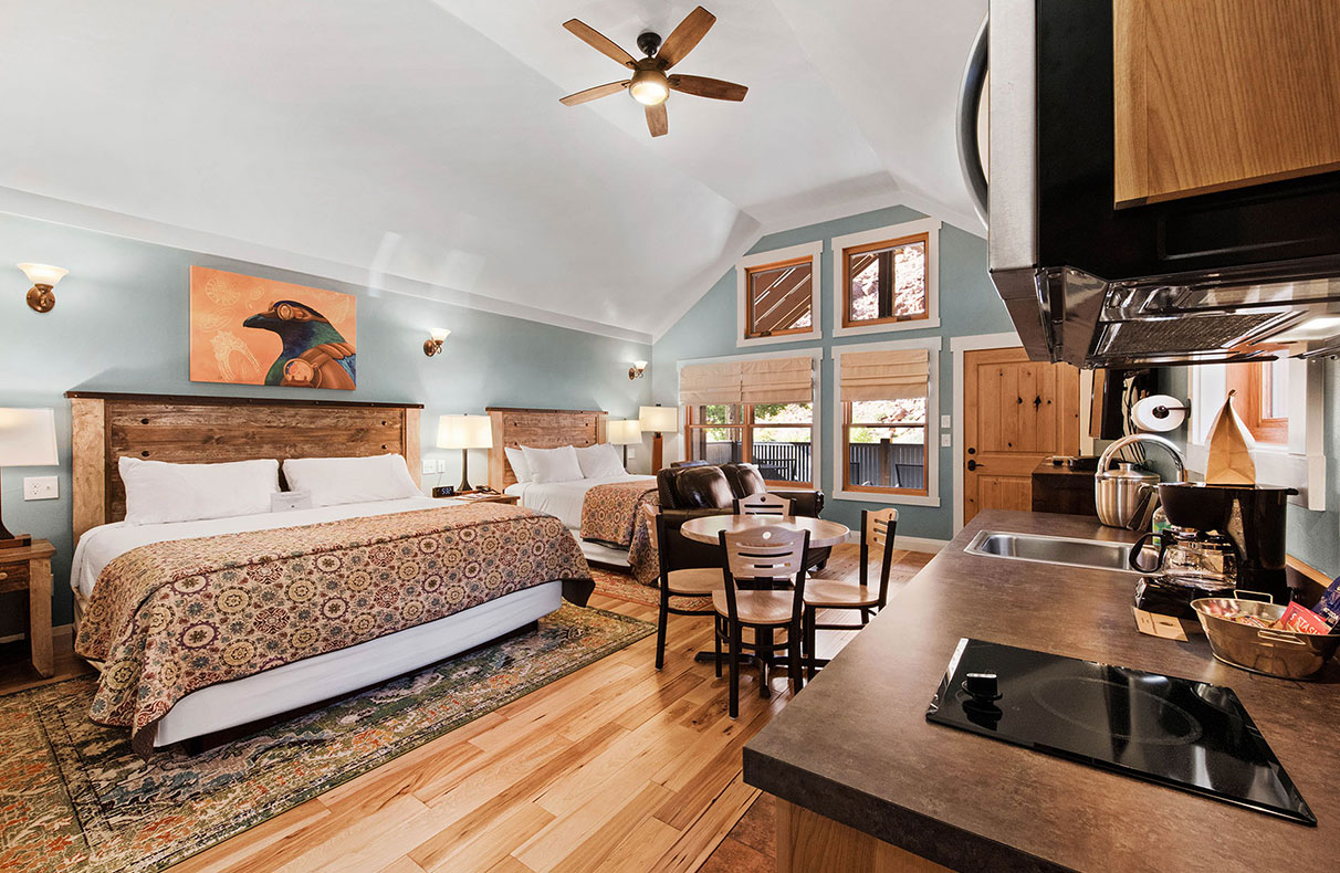 The bedroom of Unit #19 at Moab Springs Ranch is furnished with a king sized bed with a circular geometric print cover, a solid brown wood headboard and white bedside tables.