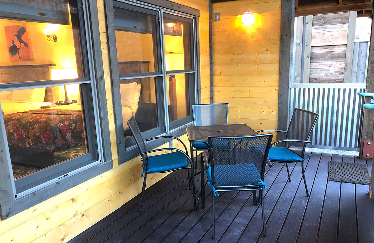 The outdoor space of a housing unit on Moab Springs Ranch has sturdy metal chairs and table, a black woodburning fireplace, barbecue and corrugated metal enclosure.