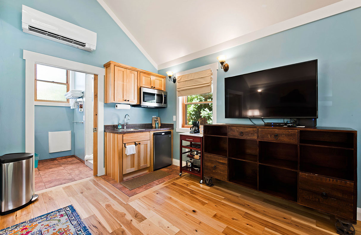 The sitting area of Unit #18 at Moab Springs Ranch is furnished with two grey fabric covered armchairs, a floor lamp, two red leather ottomans, and a wall mounted flatscreen TV.