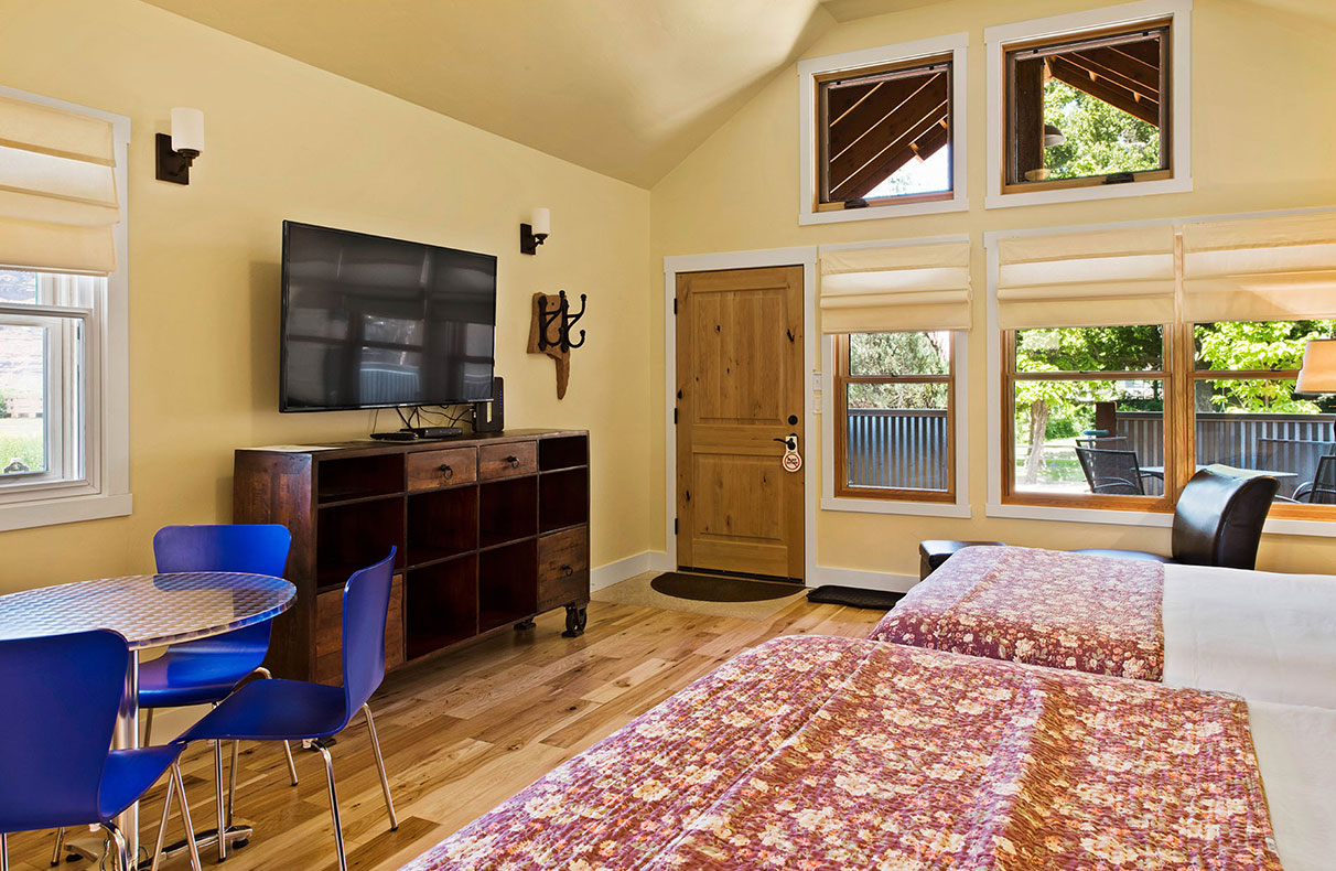 A black wood framed queen sized bed, covered in a multi-colored geographical print is presented with three large white pillows at a bedroom suite in Unit #21 at Moab Springs Ranch.