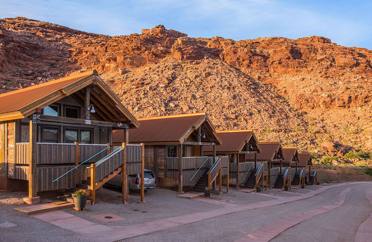 Rows of triangular rooftops of townhouses at Moab Springs Ranch are set against the background of sandcliffs, pale green grasslands and tall lush cottonwood trees.