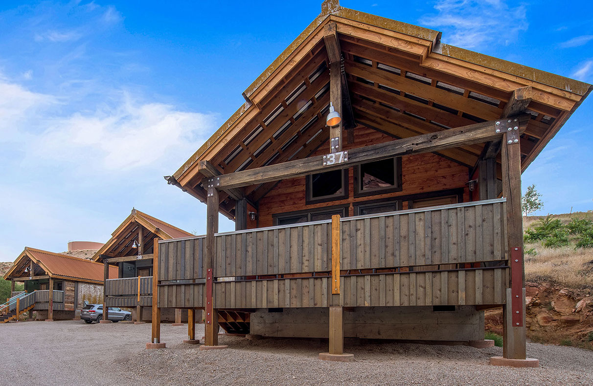 The outdoor lounging area of townhomes at Moab Springs Ranch faces a shallow stream, vibrant green grassland and towering cottonwood trees.